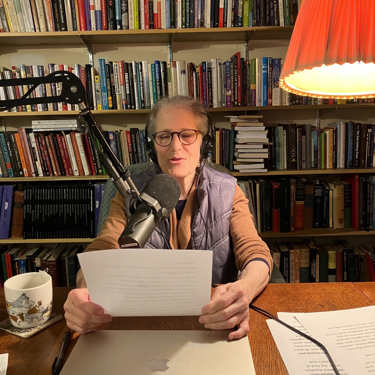Dr. Zoh in a studio recording a podcast. A library of books is behind her and she is holding a paper that she is reading from.